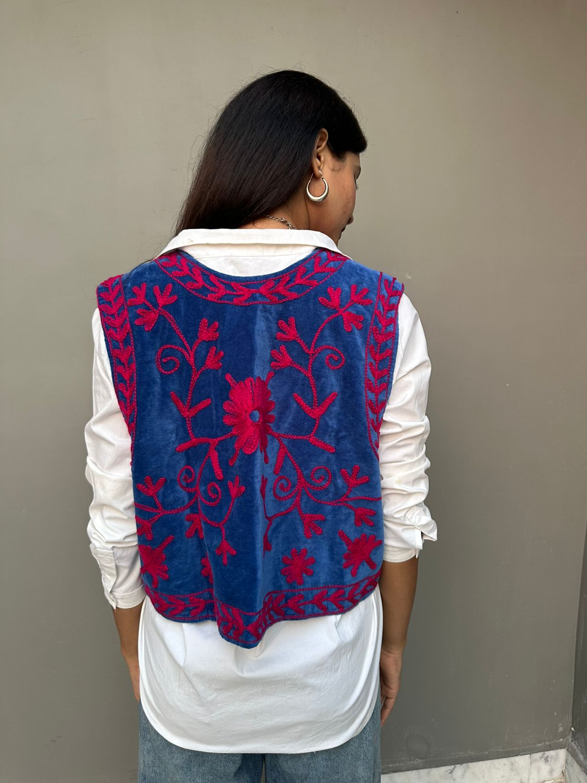 Blue embroidered vest with pink patterns over a white shirt against a plain background
